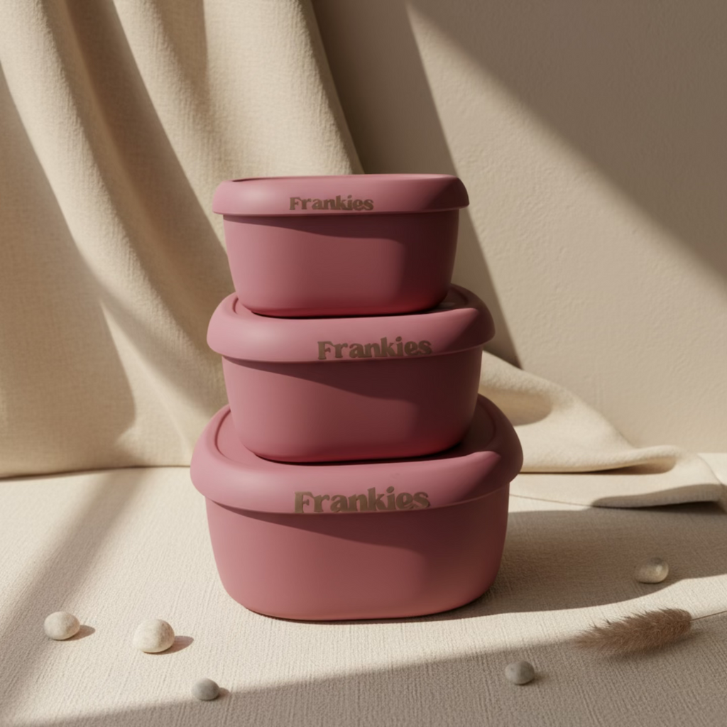 Three pink food storage containers with 'Frankies' written on the lids, stacked on top of each other.